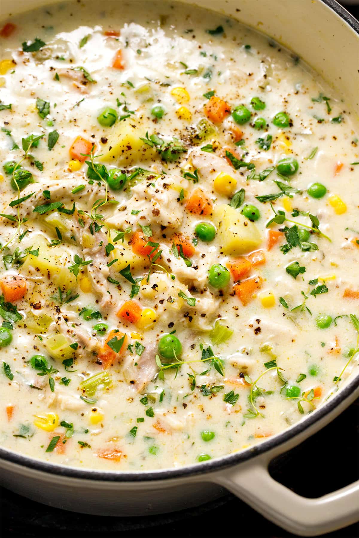 Chicken Pot Pie Soup A pot of creamy chicken soup with shredded chicken, peas, corn, carrots, potatoes, celery, and fresh herbs, topped with cracked black pepper.