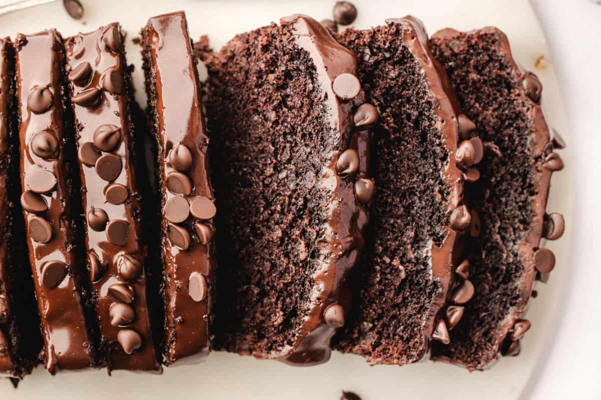 Sliced chocolate loaf cake topped with glossy chocolate glaze and sprinkled with chocolate chips.