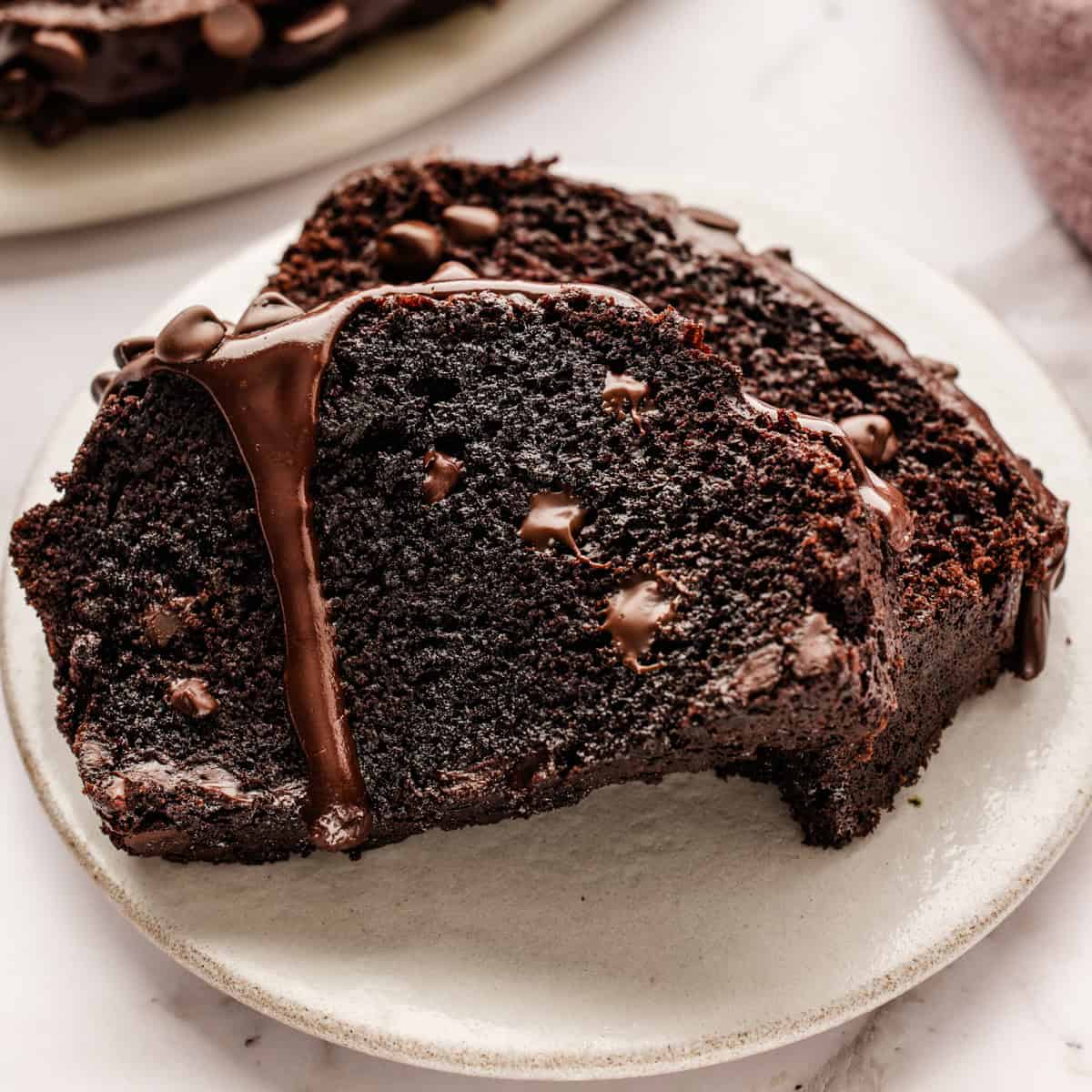 Chocolate Loaf Cake Two thick slices of moist chocolate bread with chocolate chips and a drizzle of melted chocolate on top, served on a white plate.