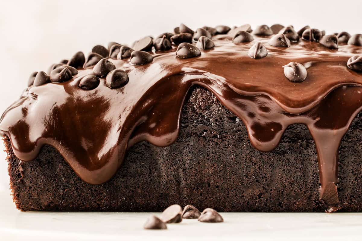 A close-up of a rich chocolate cake topped with glossy chocolate ganache and scattered chocolate chips.