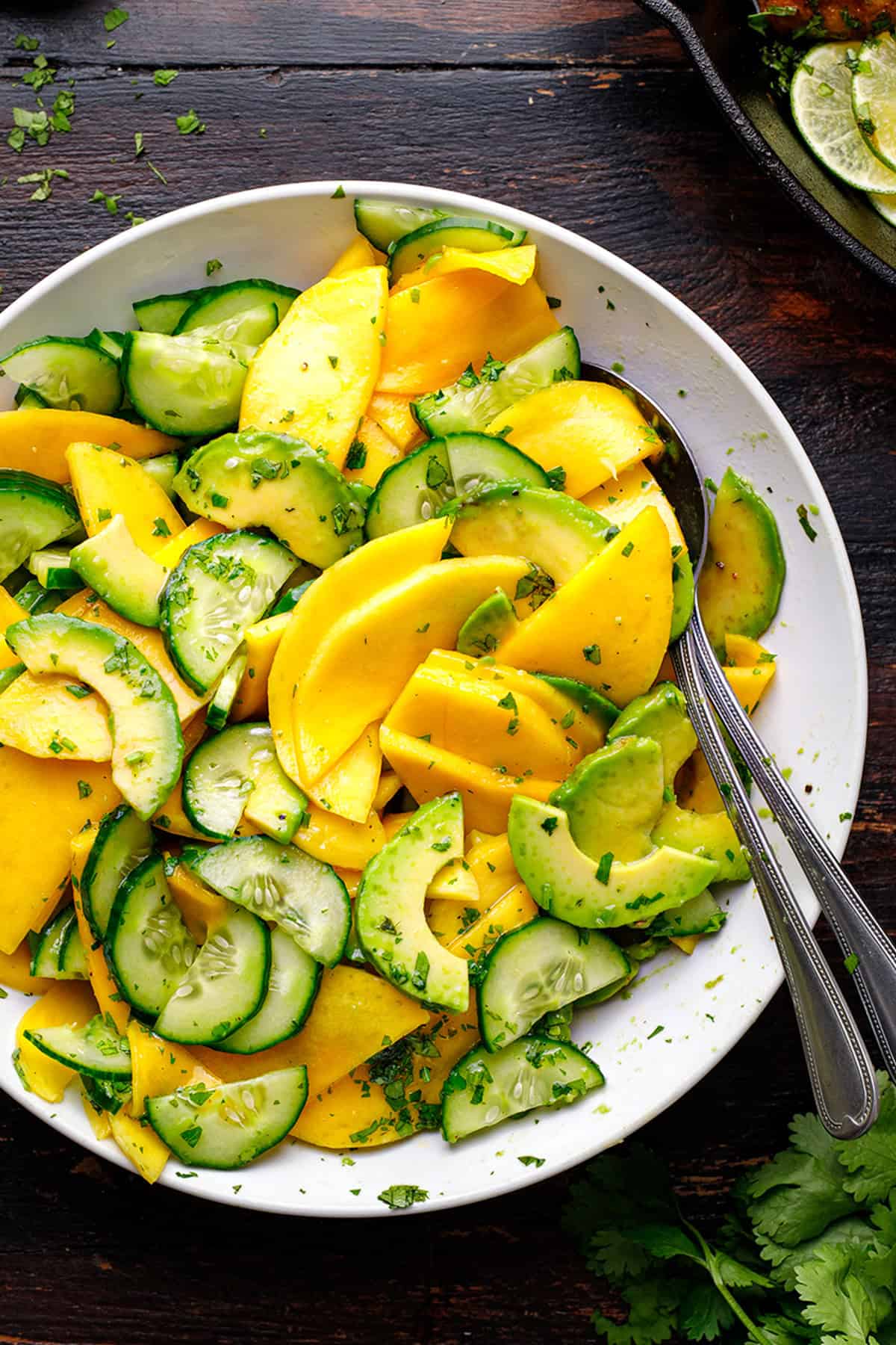 Grilled Cilantro Lime Chicken Thighs A white bowl filled with sliced mango, cucumber, and avocado, garnished with chopped herbs.