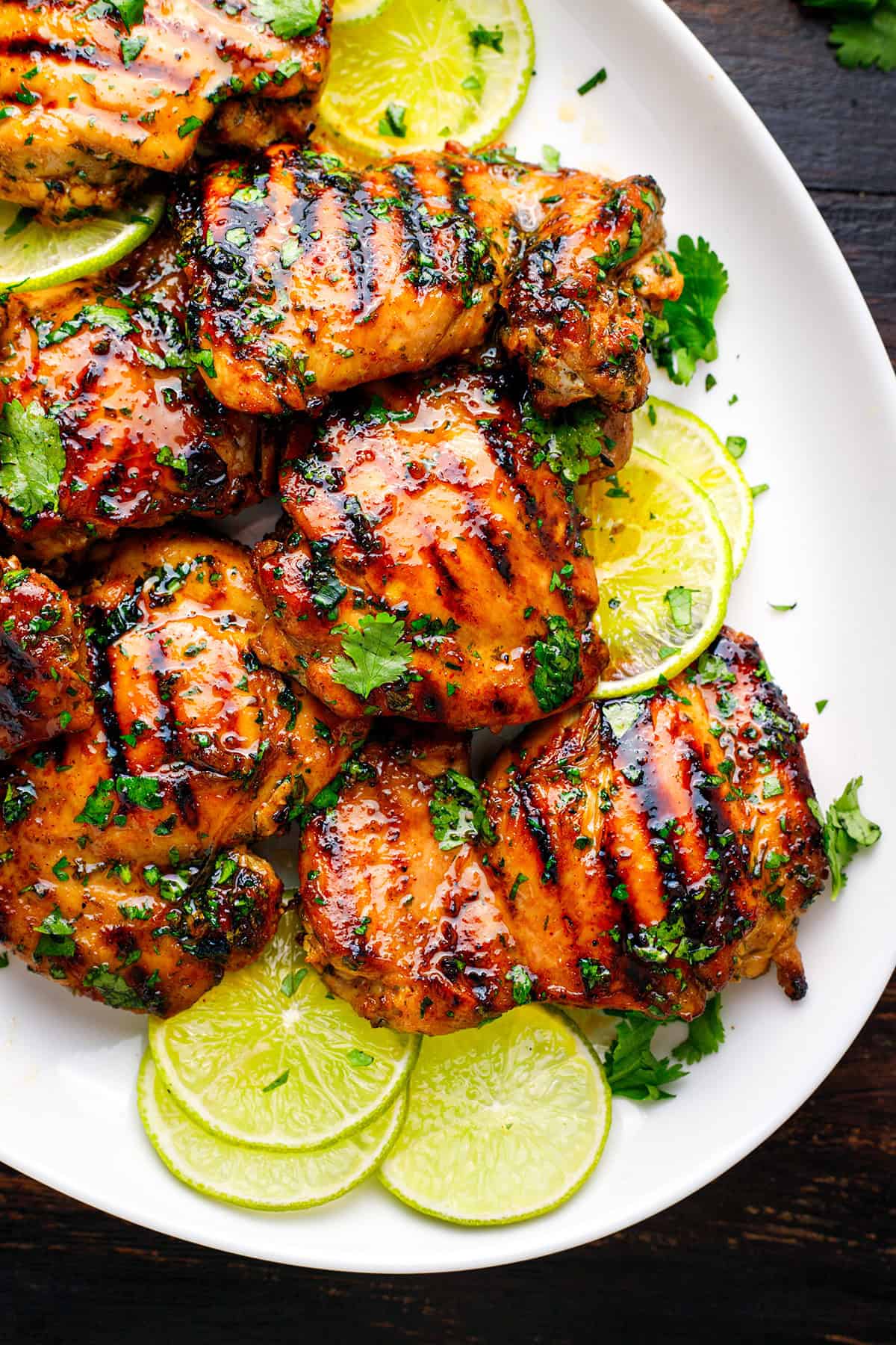 Cilantro-Lime Chicken Thighs Grilled chicken thighs garnished with chopped cilantro served on a white plate with fresh lime slices. The chicken has char marks and a glazed appearance.