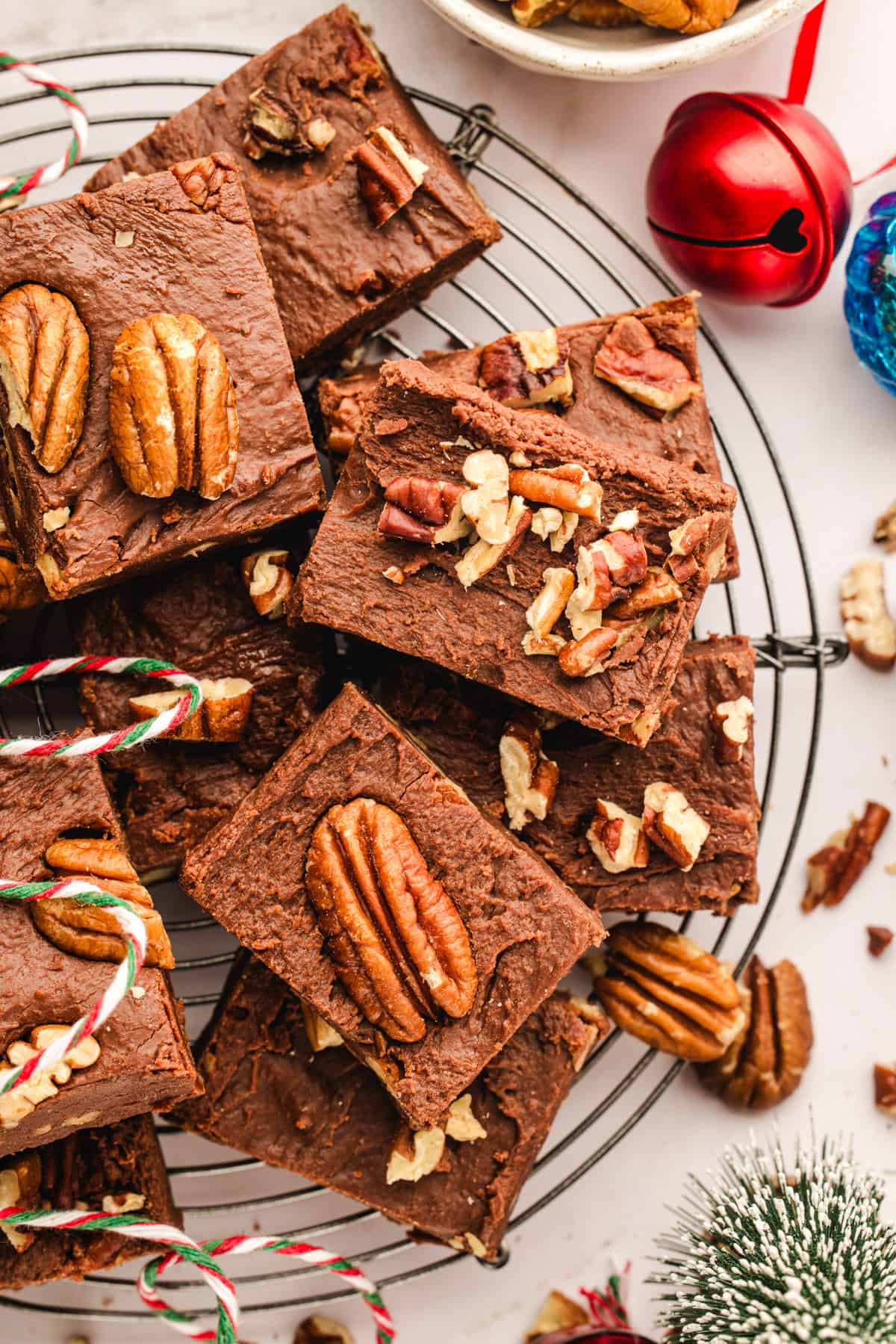 Fantasy Fudge Chocolate fudge topped with pecans are stacked on a round cooling rack.