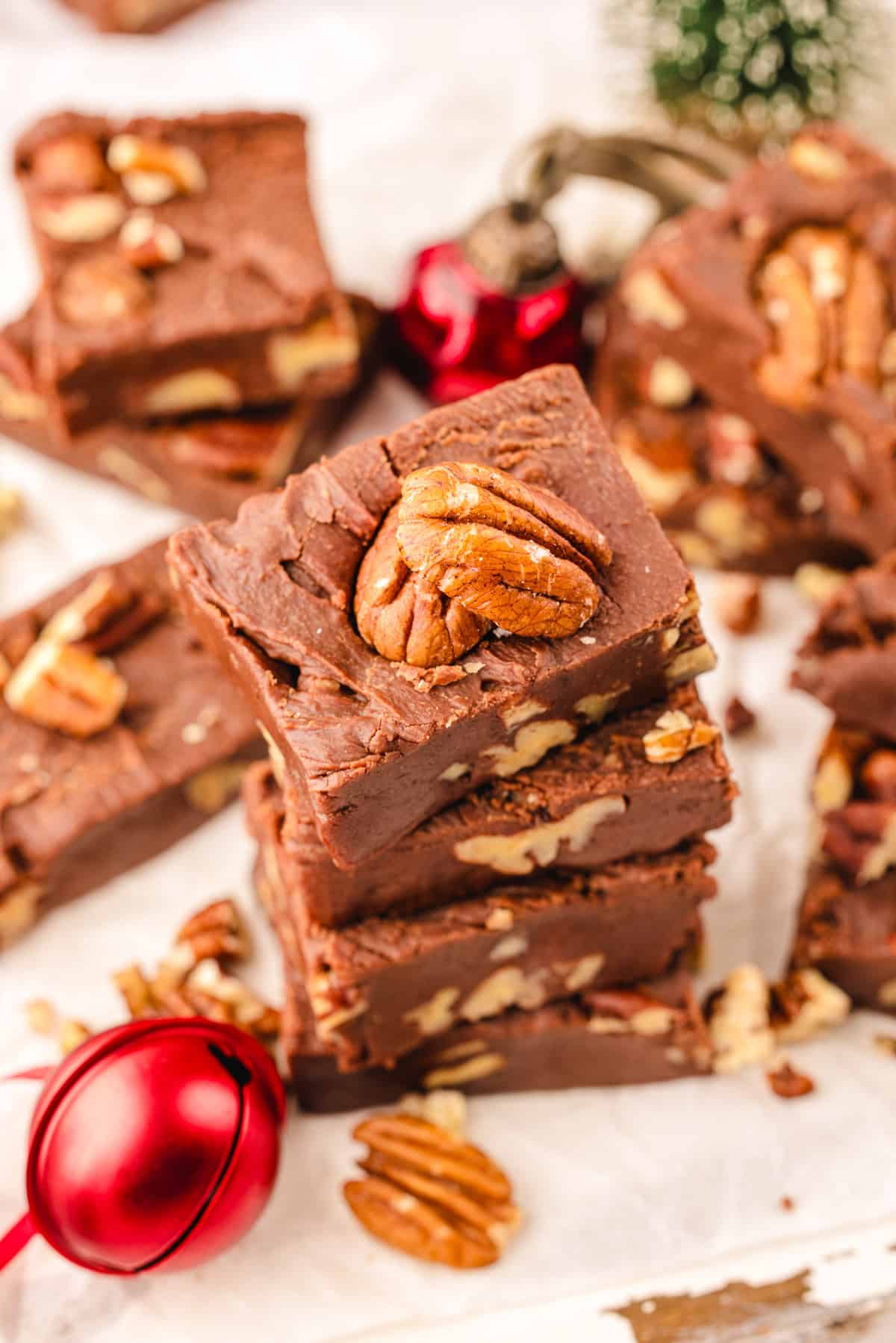Fantasy Fudge A stack of chocolate fudge squares with pecans on top and scattered around, placed on parchment paper.