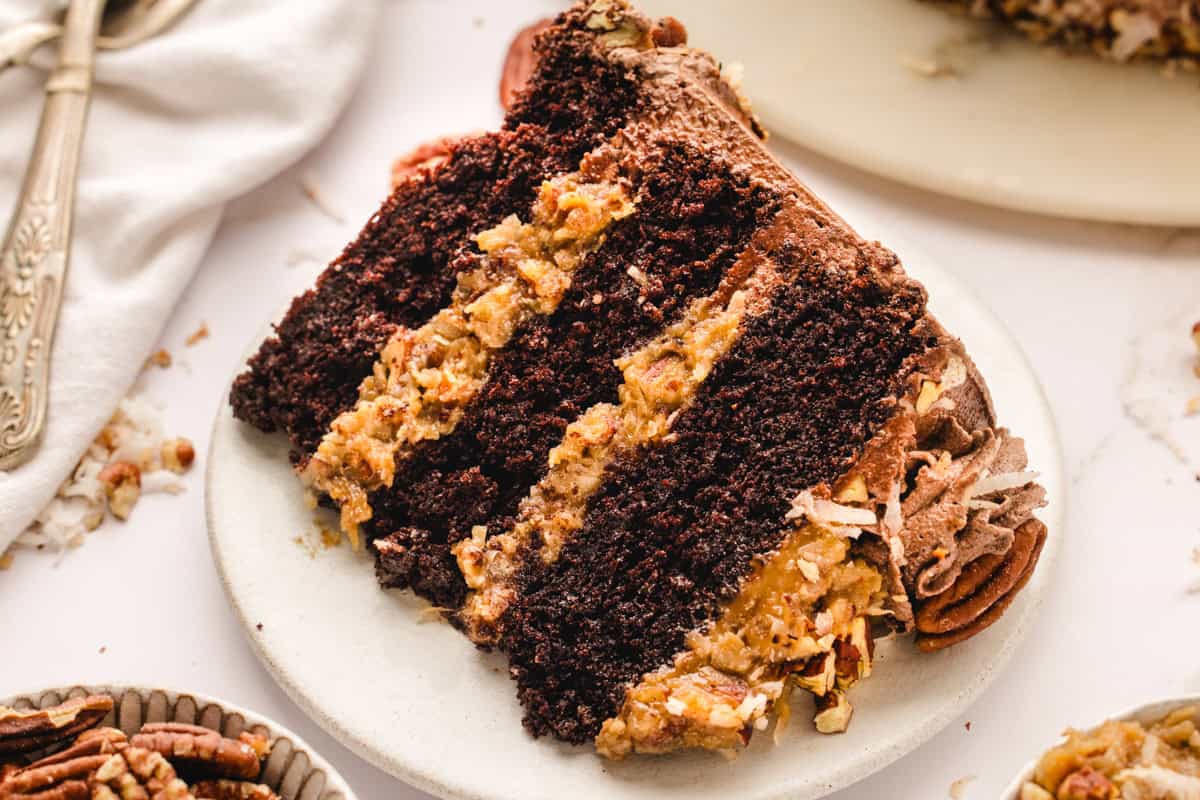 German Chocolate Cake A slice of German chocolate cake with layers of chocolate cake and coconut-pecan filling on a white plate.