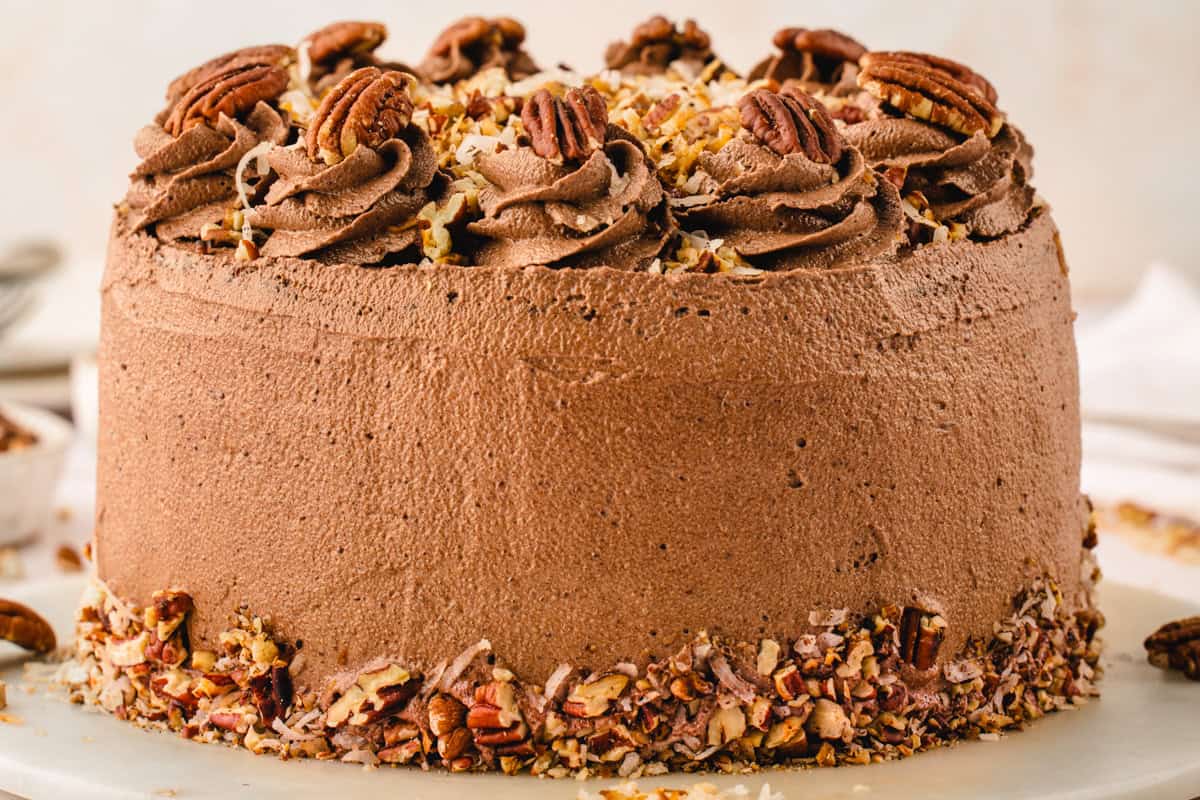 German Chocolate Cake A round chocolate cake with chocolate frosting, topped with pecans and chopped nuts, and decorated with swirls of frosting.