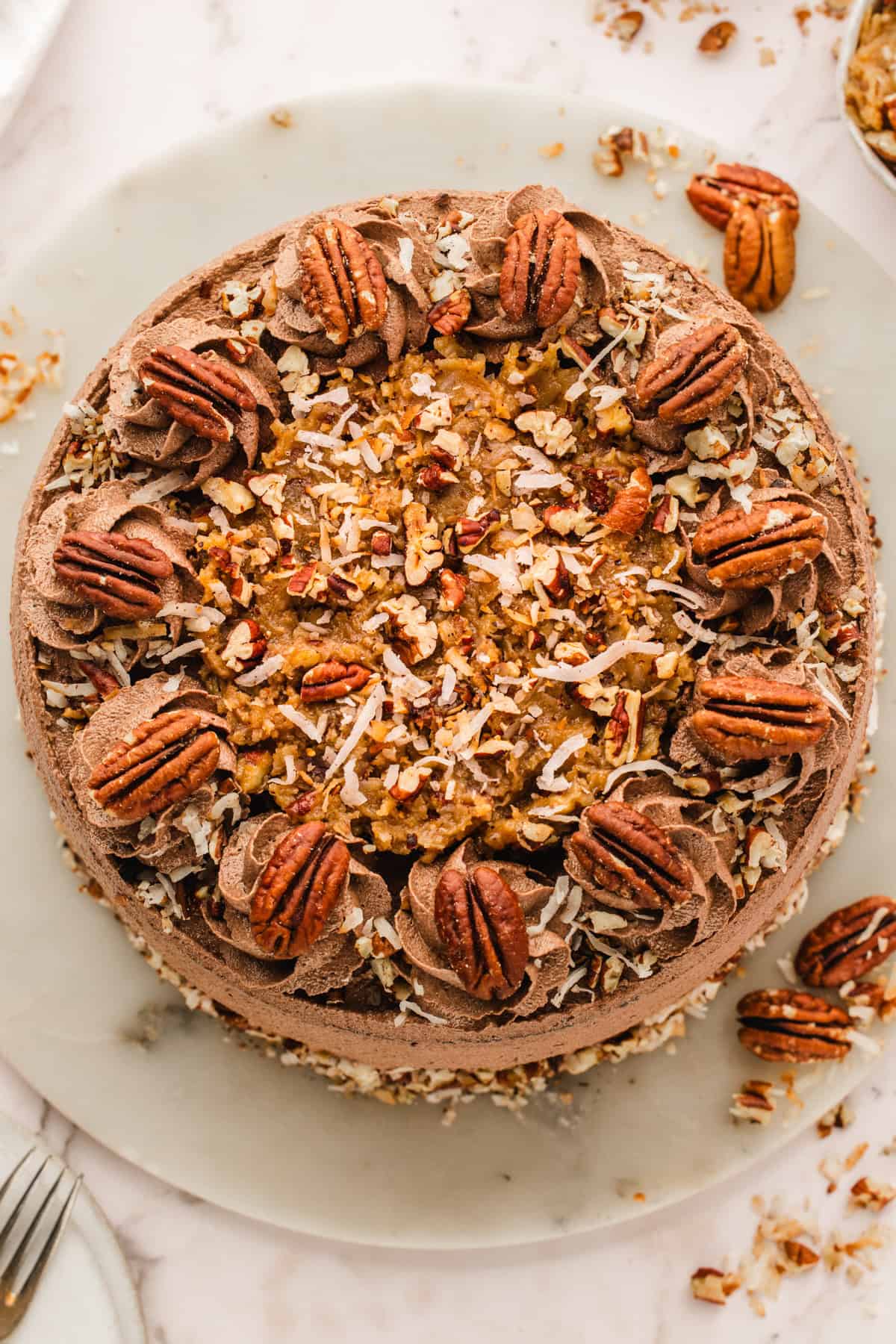 German Chocolate Cake A round German chocolate cake topped with chocolate frosting swirls, pecans, shredded coconut, and chopped nuts.