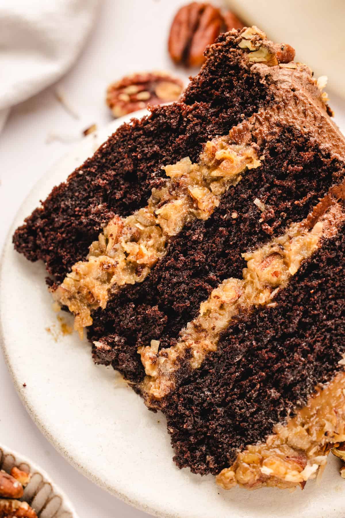 German Chocolate Cake A close-up of a slice of German chocolate cake with rich chocolate layers and coconut-pecan filling, served on a white plate.