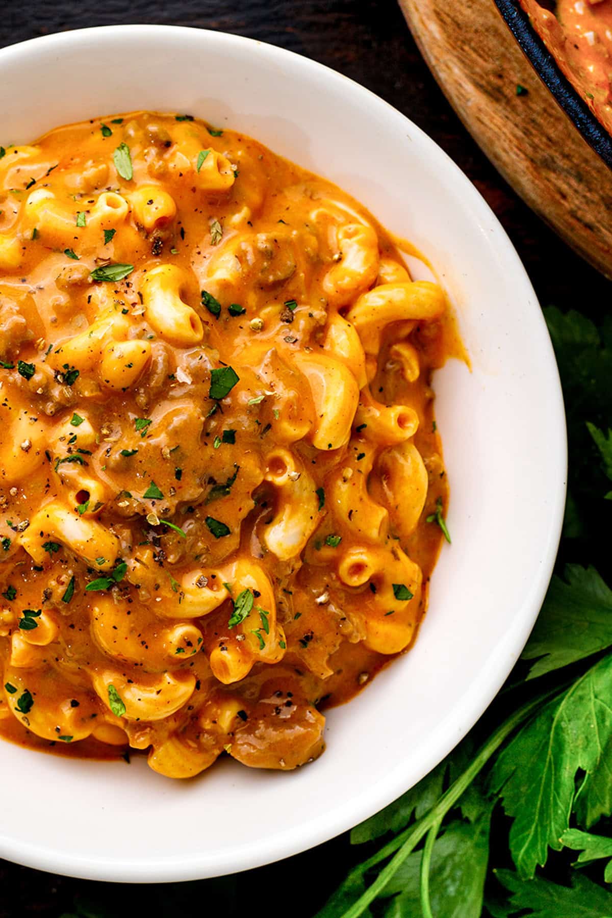Hamburger Helper A white bowl filled with creamy macaroni and ground beef in a rich, tomato sauce, garnished with chopped parsley.