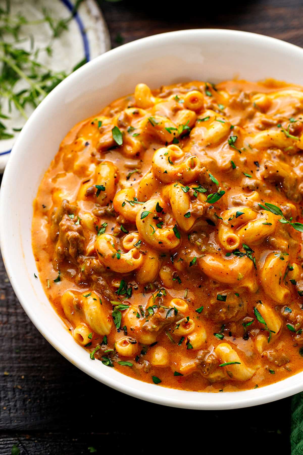 Hamburger Helper A white bowl filled with creamy, cheesy macaroni and beef in a rich tomato sauce, garnished with chopped herbs.