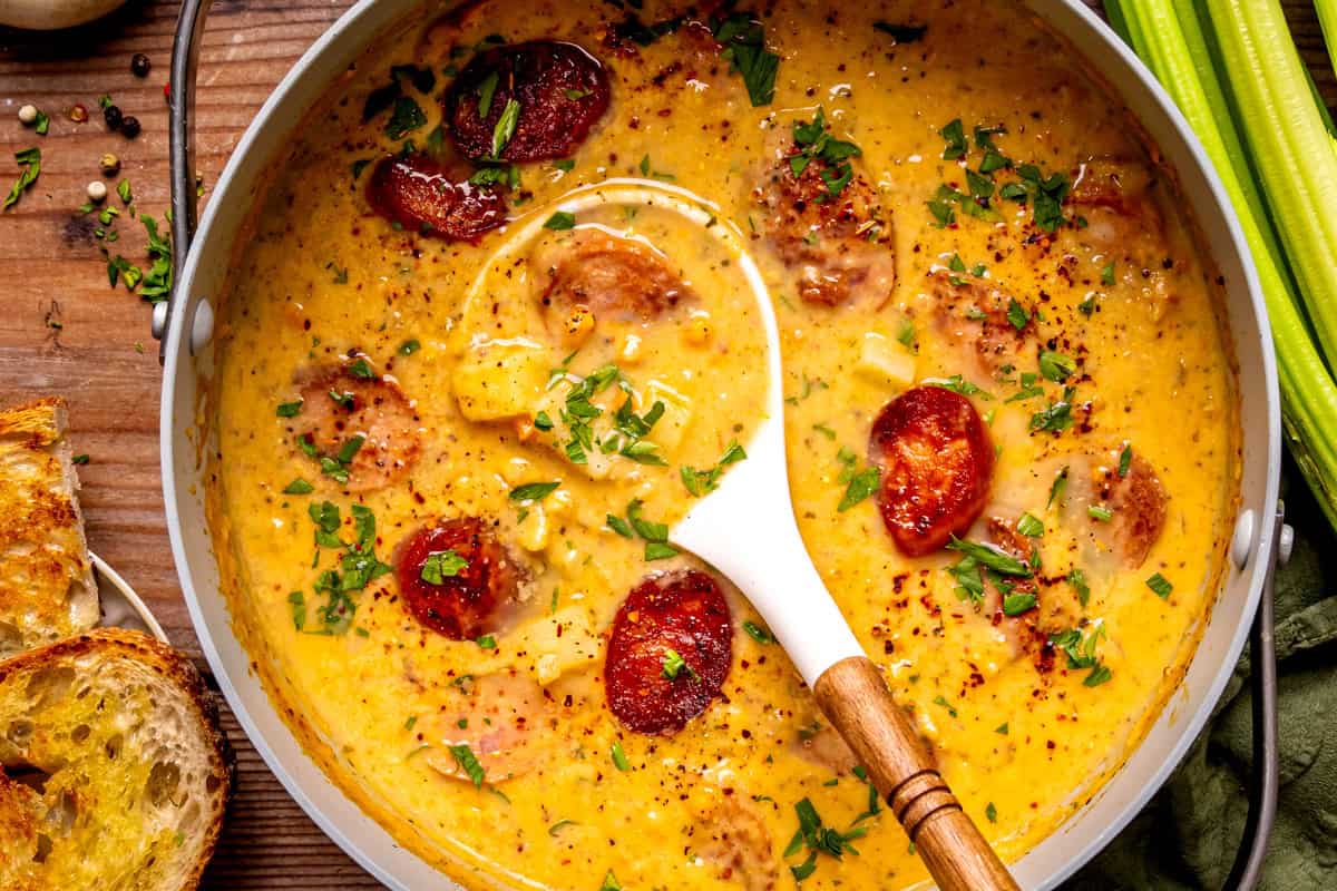 Kielbasa Potato Soup A pot of creamy yellow soup with sliced sausage, herbs, and spices, garnished with chopped parsley.