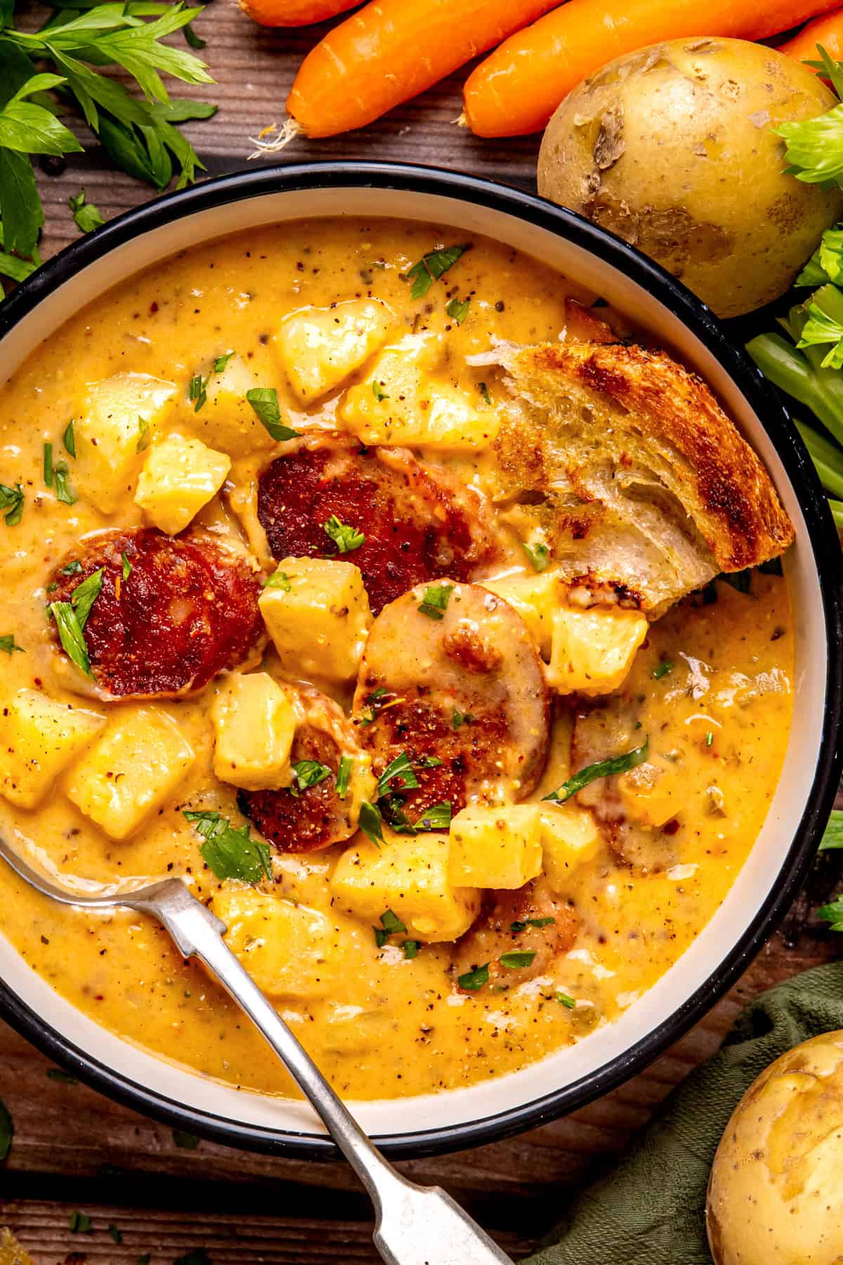 Kielbasa Potato Soup A bowl of creamy sausage and potato soup, topped with fresh herbs, diced potatoes, and crispy bread.