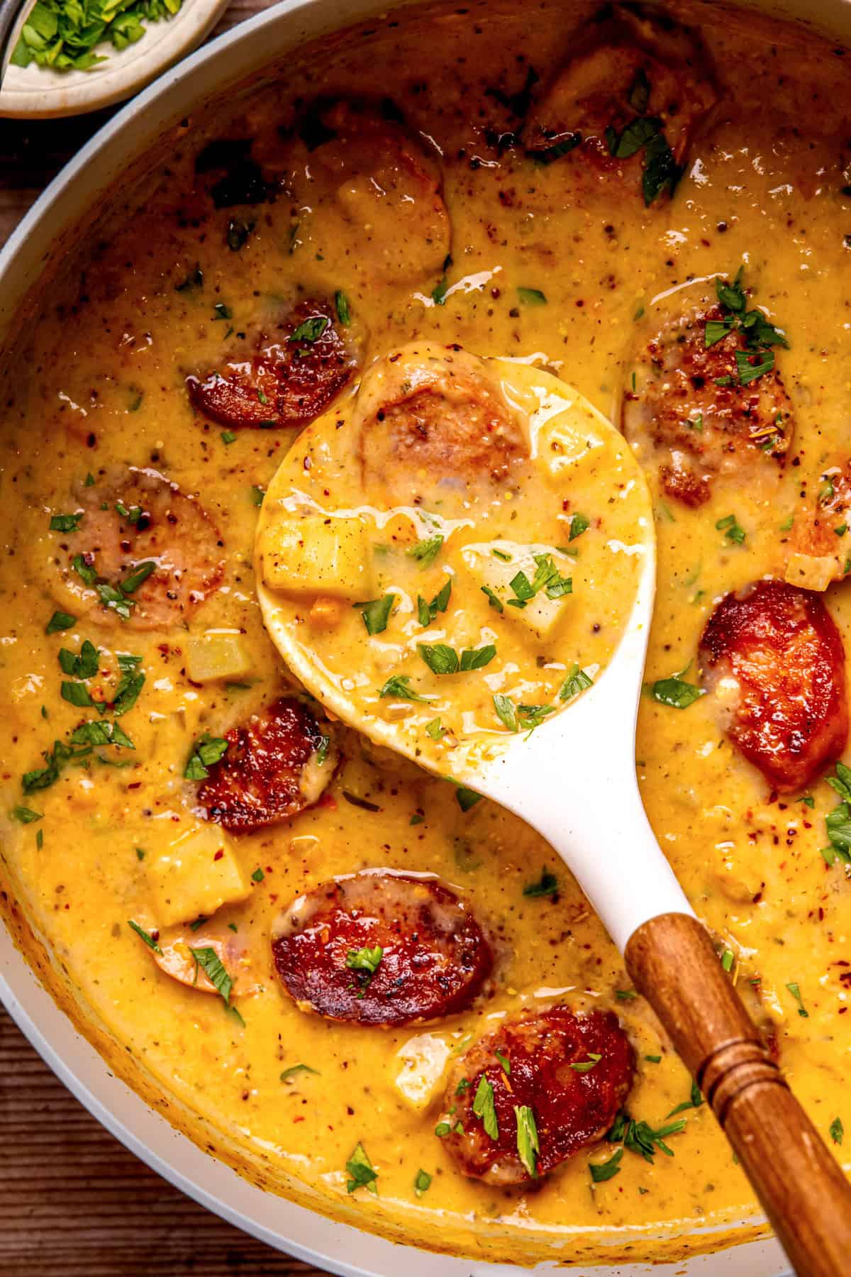 Kielbasa Potato Soup A creamy, yellow sauce with browned sausage slices and herbs in a pan.