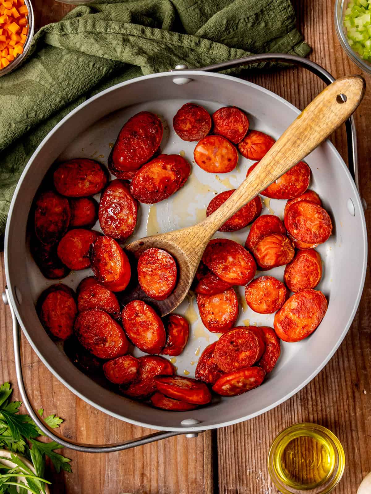 Kielbasa Potato Soup Sliced, browned chorizo sausage cooking in a large skillet with a wooden spoon.