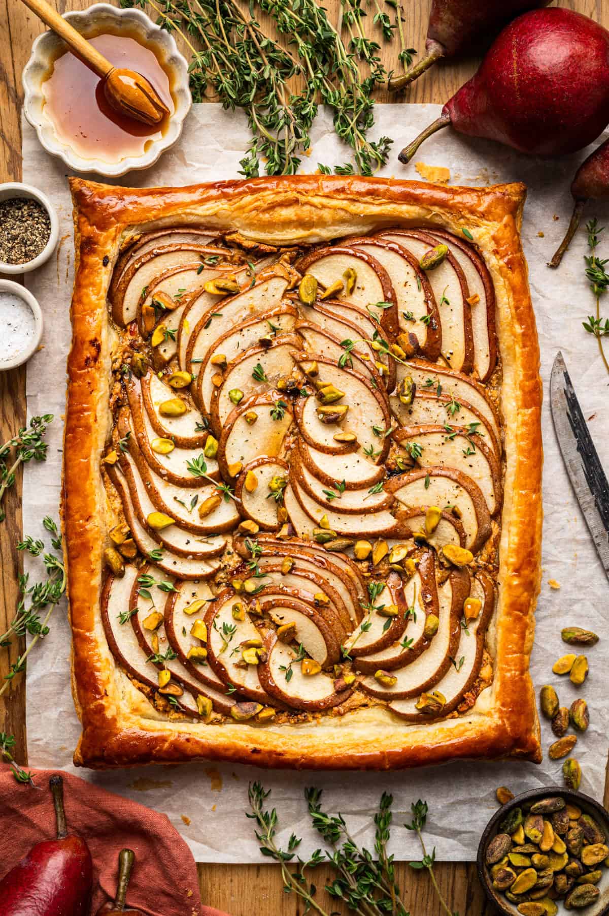 Pear Tart A rectangular pear tart with layered pear slices, pistachios, fresh thyme, and honey on puff pastry.