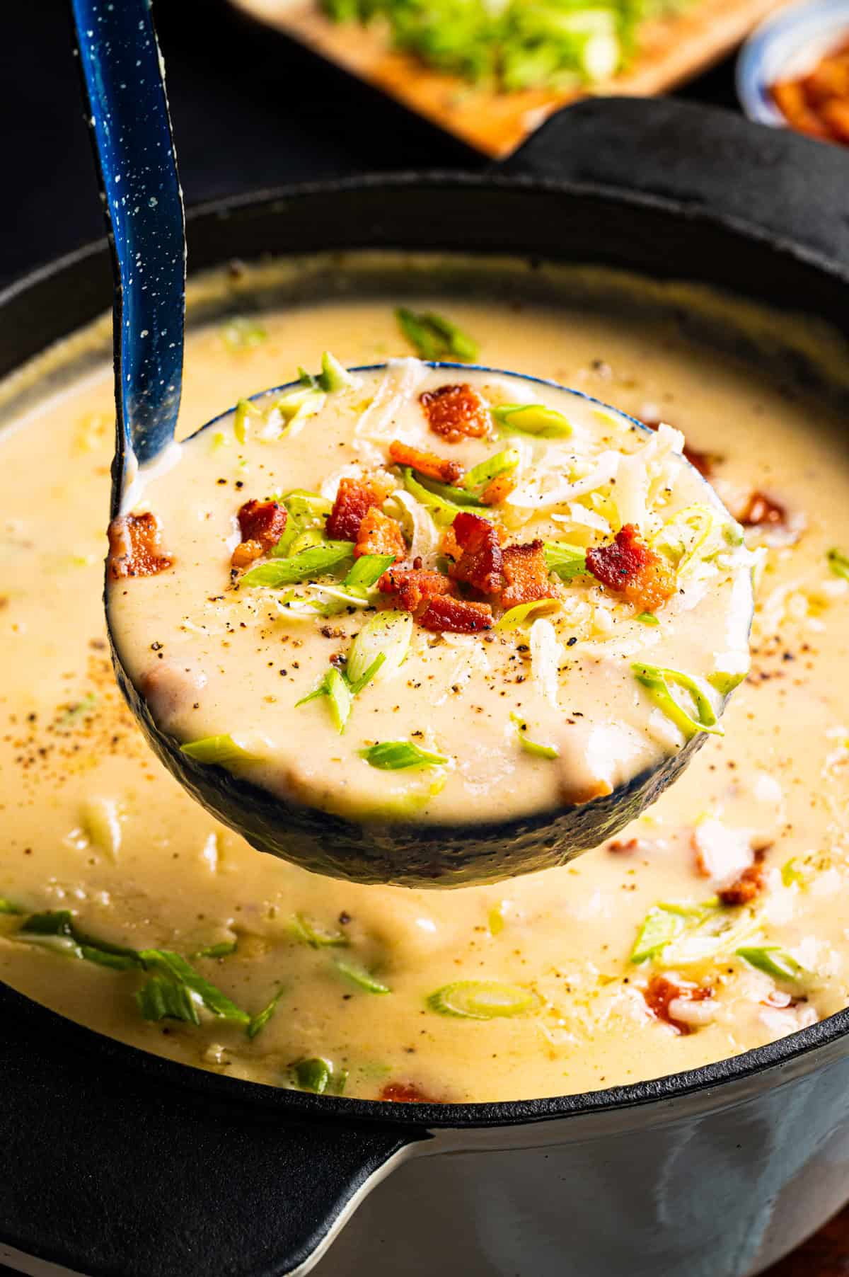 Creamy Potato Soup with Bacon and Cheddar A ladle lifts creamy potato soup from a pot, topped with chopped green onions, shredded cheese, and crispy bacon bits.