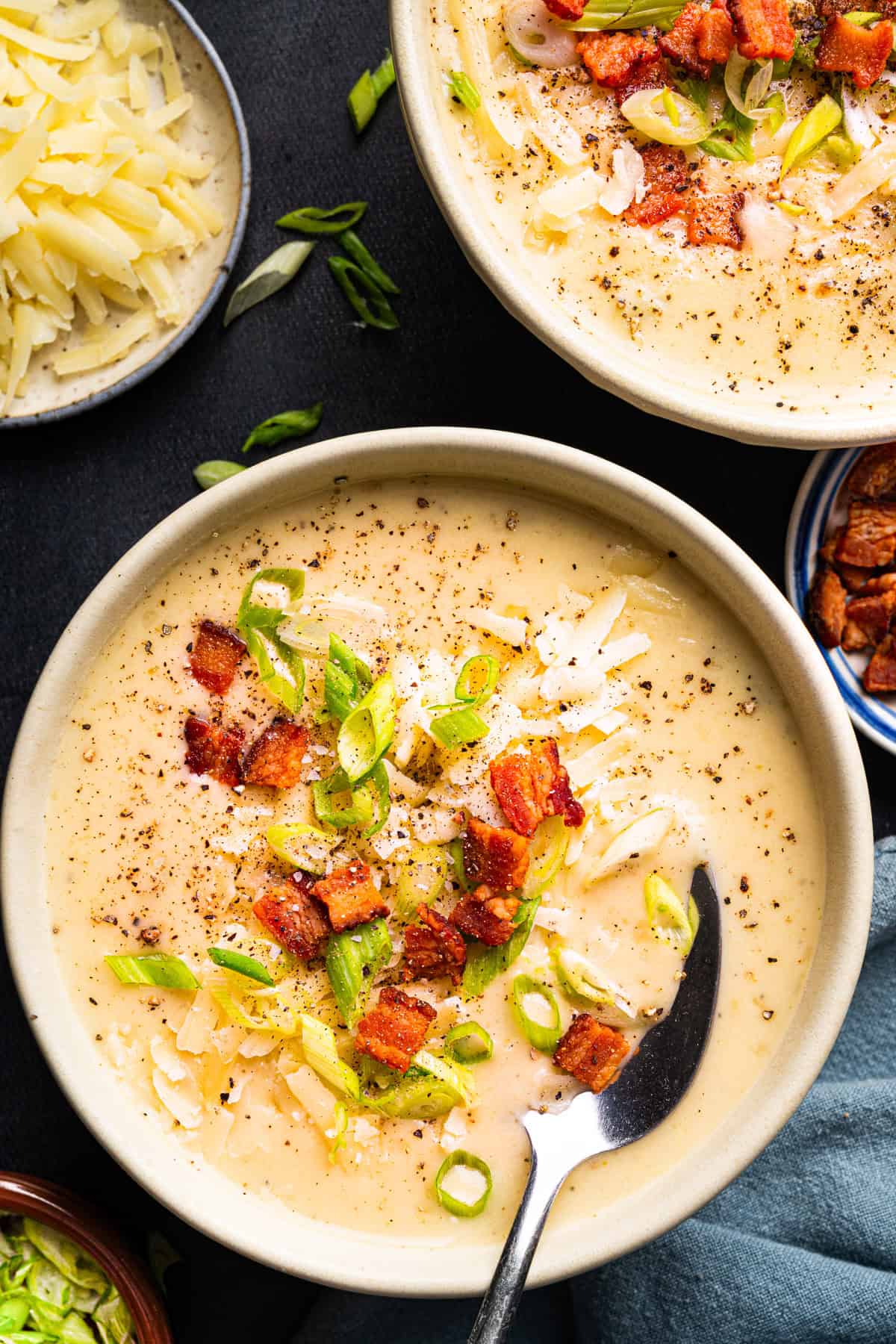 Creamy Potato Soup with Bacon and Cheddar A bowl of creamy potato soup topped with shredded cheese, crispy bacon, chopped green onions, and black pepper, with a spoon resting in the bowl.