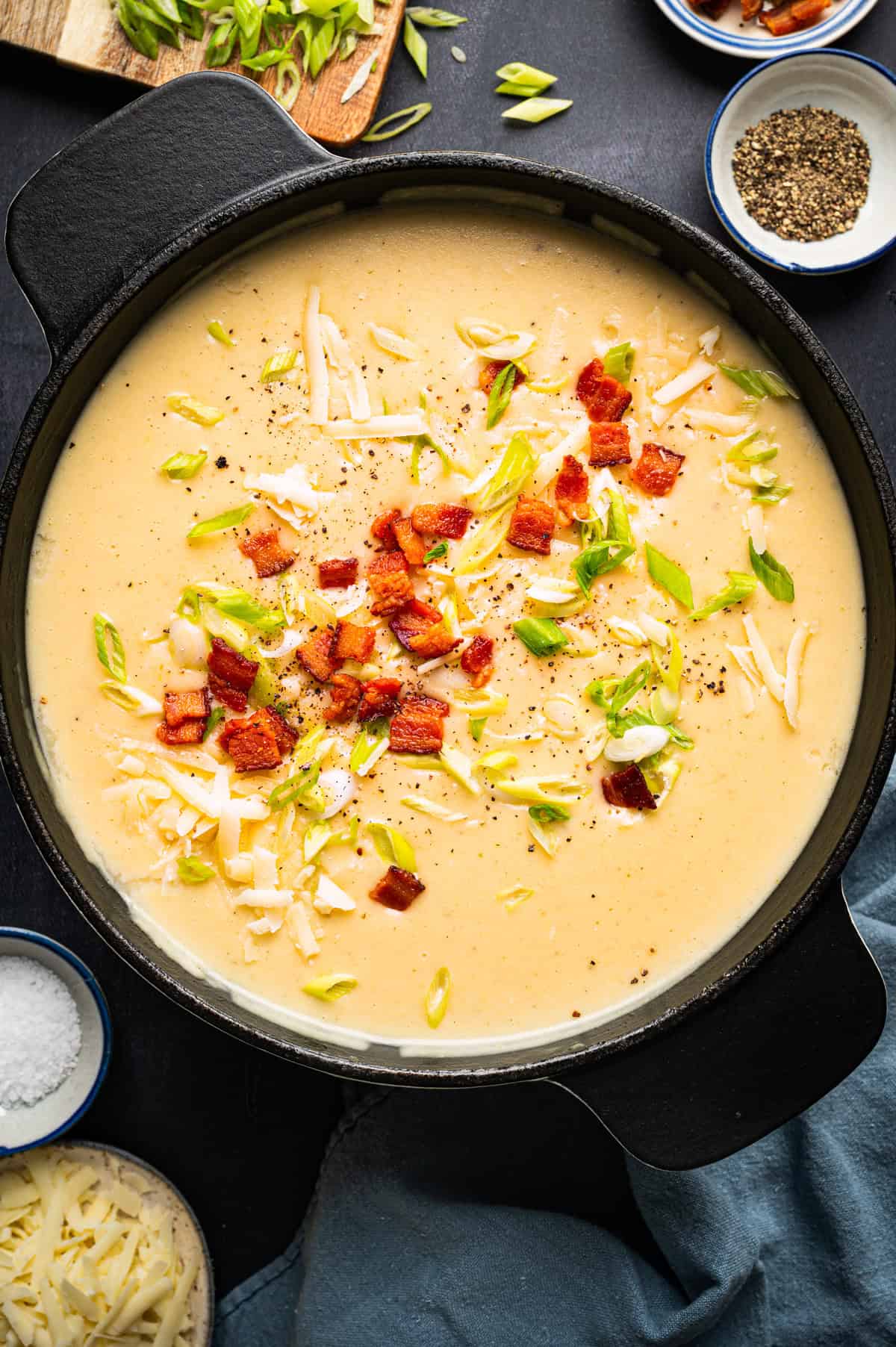 Creamy Potato Soup with Bacon and Cheddar Creamy potato soup in a black pot topped with shredded cheese, bacon pieces, chopped green onions, and black pepper.