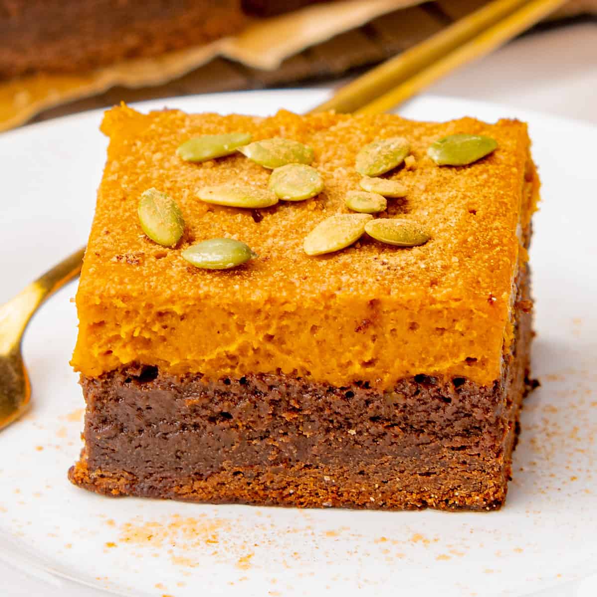 Pumpkin Brownies A slice of layered dessert with a chocolate base and orange topping, garnished with pumpkin seeds.