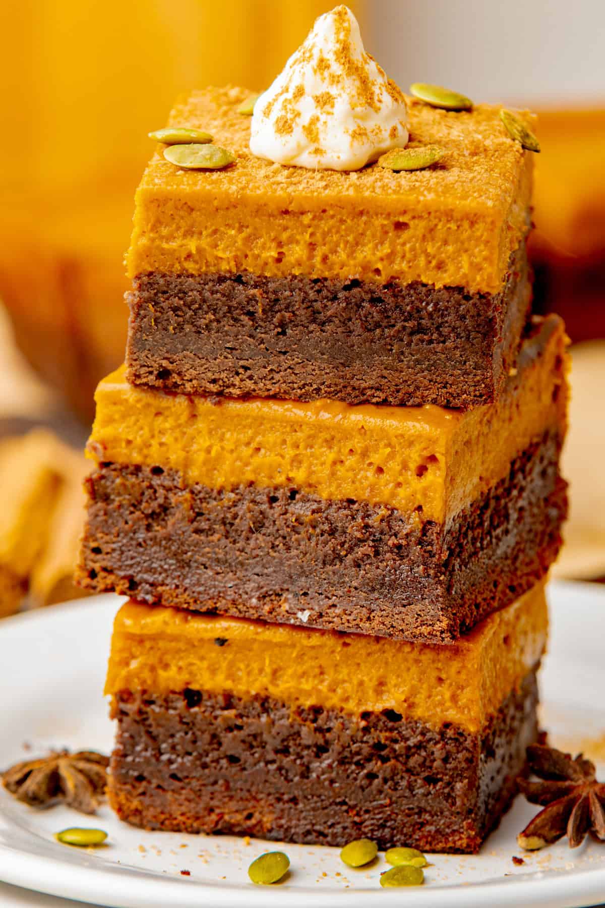 Pumpkin Brownies Three stacked pumpkin chocolate brownies topped with whipped cream and a sprinkle of spices, garnished with pumpkin seeds.