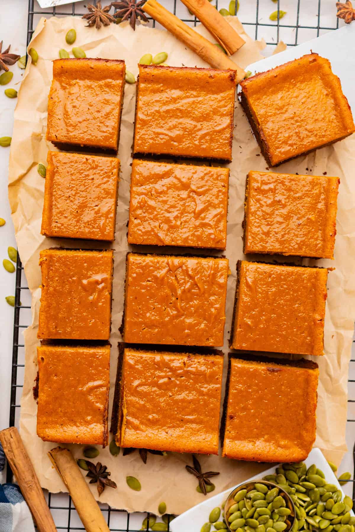 Pumpkin Brownies Twelve pumpkin bars with smooth orange tops are arranged on parchment paper over a cooling rack.