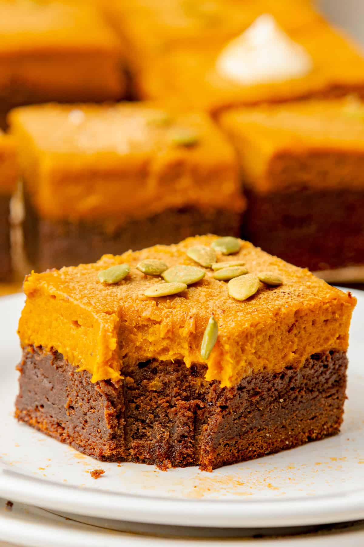 Pumpkin Brownies A close-up of a brownie topped with a thick layer of pumpkin filling and garnished with pumpkin seeds.