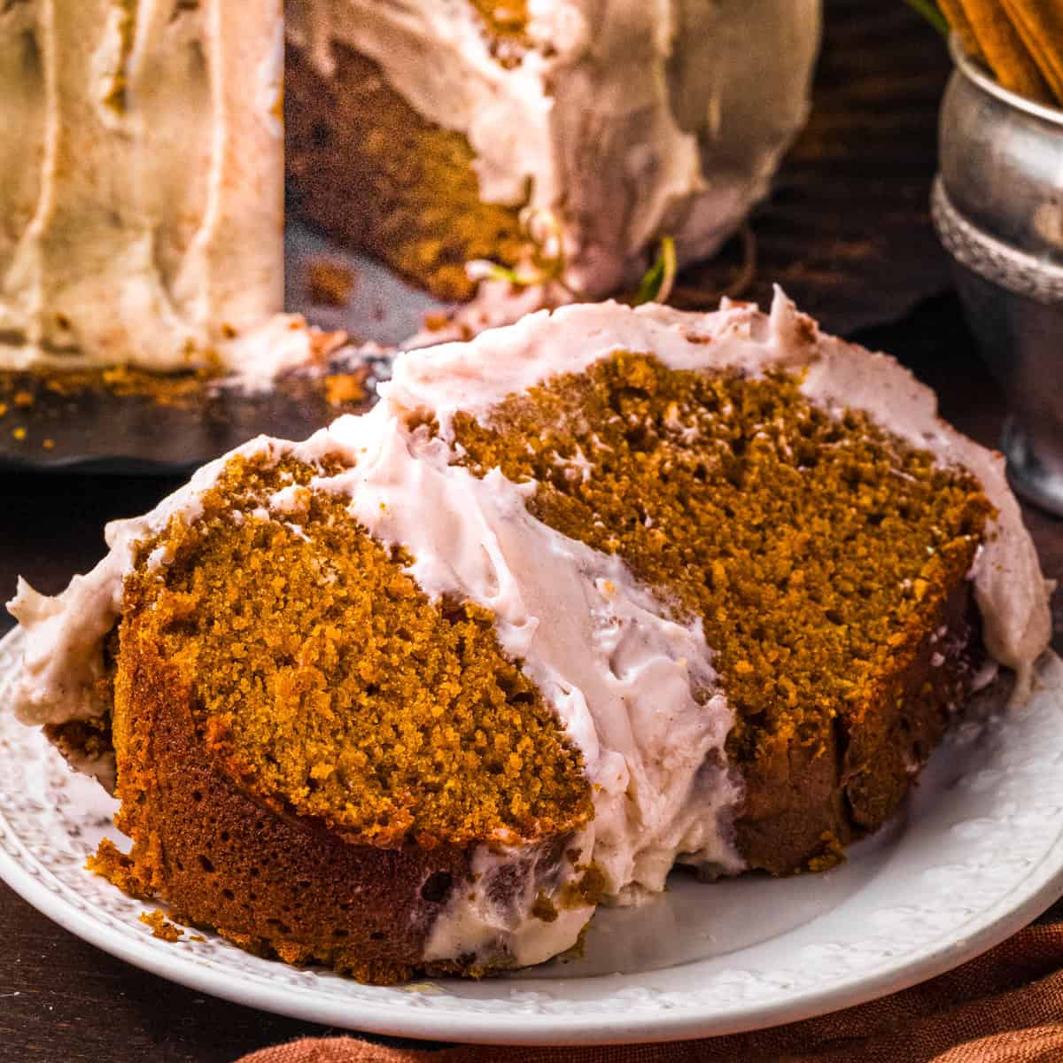 Pumpkin Cake with Cream Cheese Buttercream for Halloween and Thanksgiving Slice of moist, spiced cake with creamy frosting sit on a white plate.