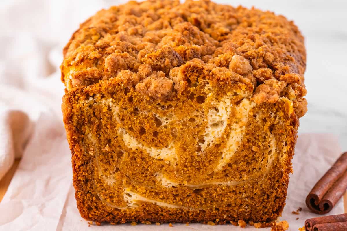 Pumpkin Cream Cheese Bread Close-up of a loaf of pumpkin bread with a crumb topping and swirl pattern inside, resting on parchment paper.