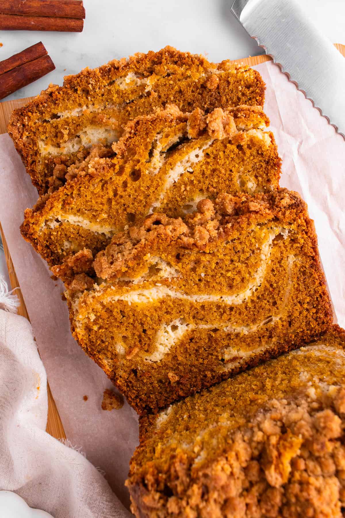 Pumpkin Cream Cheese Bread Sliced pumpkin bread with a cream cheese swirl and crumb topping on parchment paper.