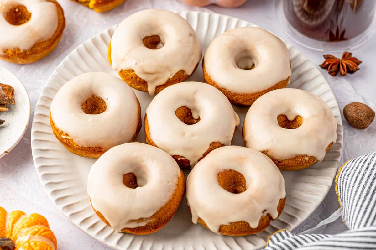 A white plate holds seven baked donuts with light glaze, arranged closely together. 