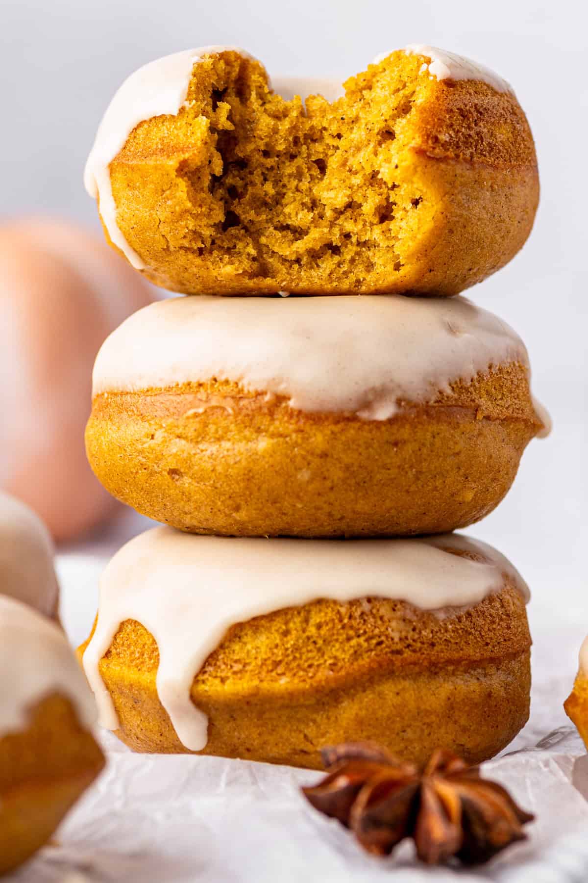 Pumpkin Spice Donuts Three pumpkin donuts with white icing are stacked. The top donut has a bite taken out, showing its moist interior.