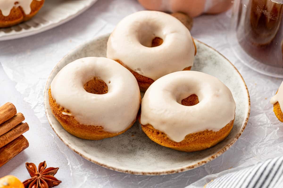 Pumpkin Spice Donuts Three baked donuts with white icing are arranged on a ceramic plate.
