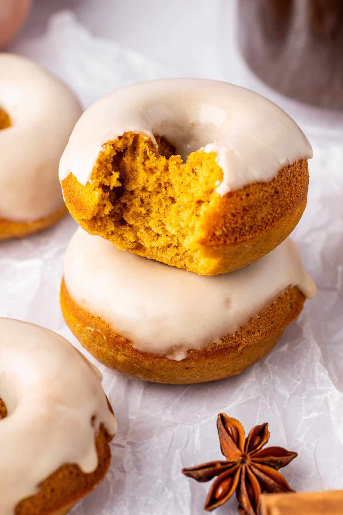 Pumpkin Spice Donuts Two pumpkin spice donuts with white glaze are stacked. The top donut has a bite taken out.