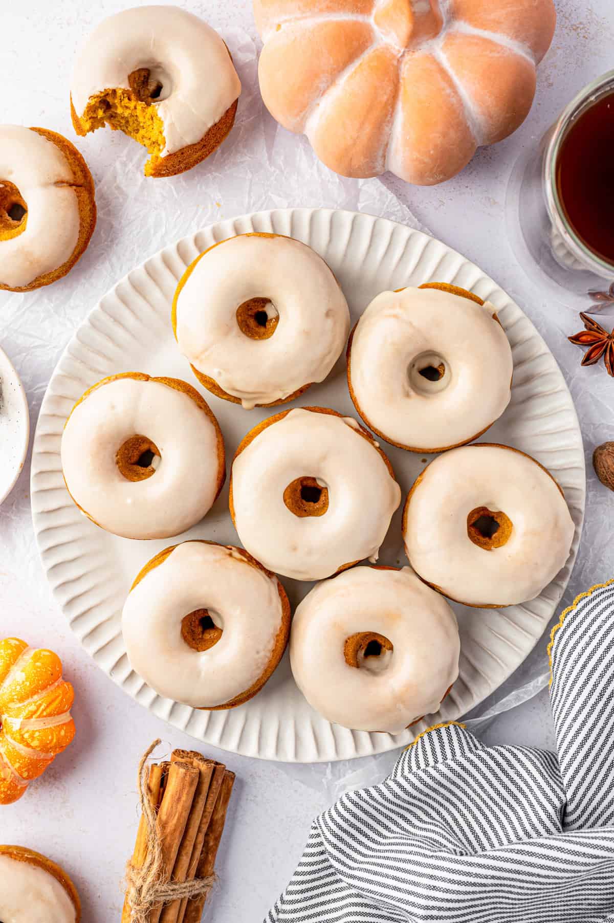 Pumpkin Spice Donuts A plate of seven glazed donuts sits on a white table.