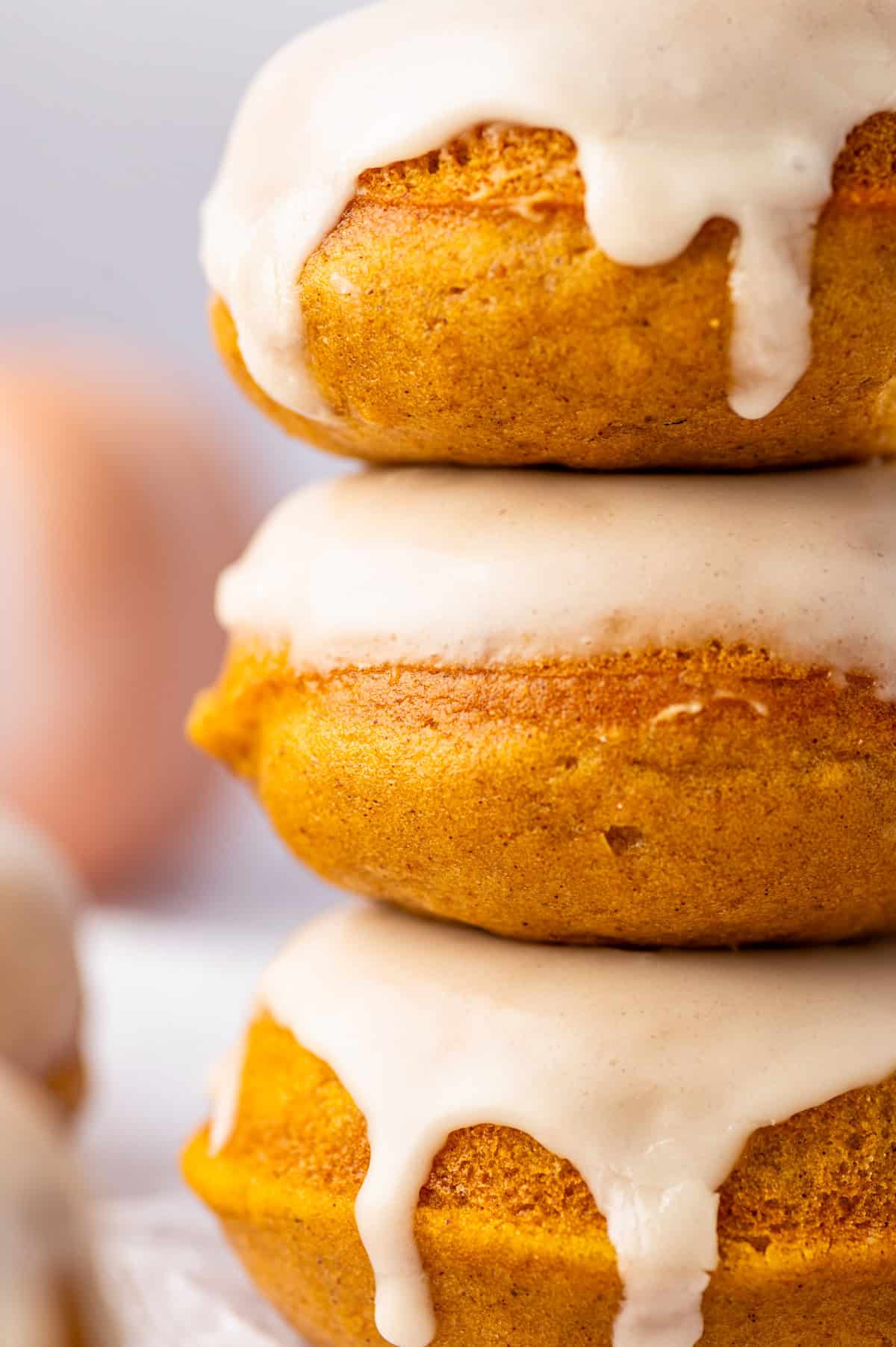 Pumpkin Spice Donuts A close-up of three stacked pumpkin donuts with a creamy glaze dripping down the sides.