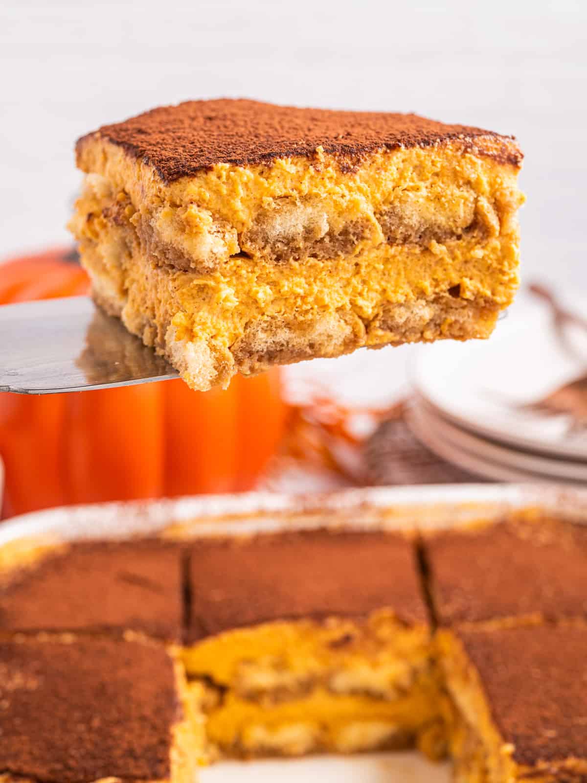 Pumpkin Tiramisu A slice of pumpkin tiramisu topped with cocoa powder is being lifted from a dish.