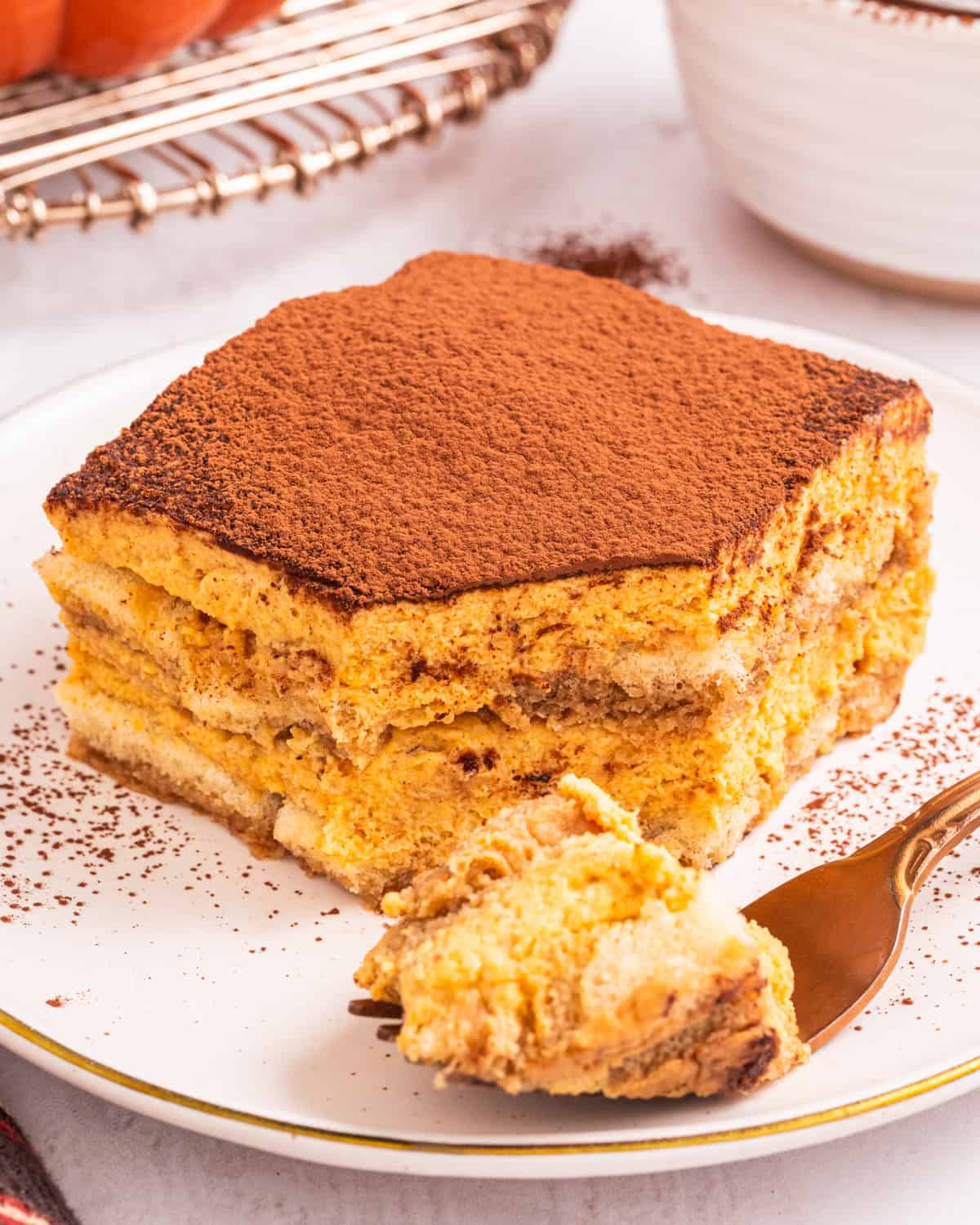 Pumpkin Tiramisu A slice of pumpkin tiramisu topped with cocoa powder sits on a white plate.