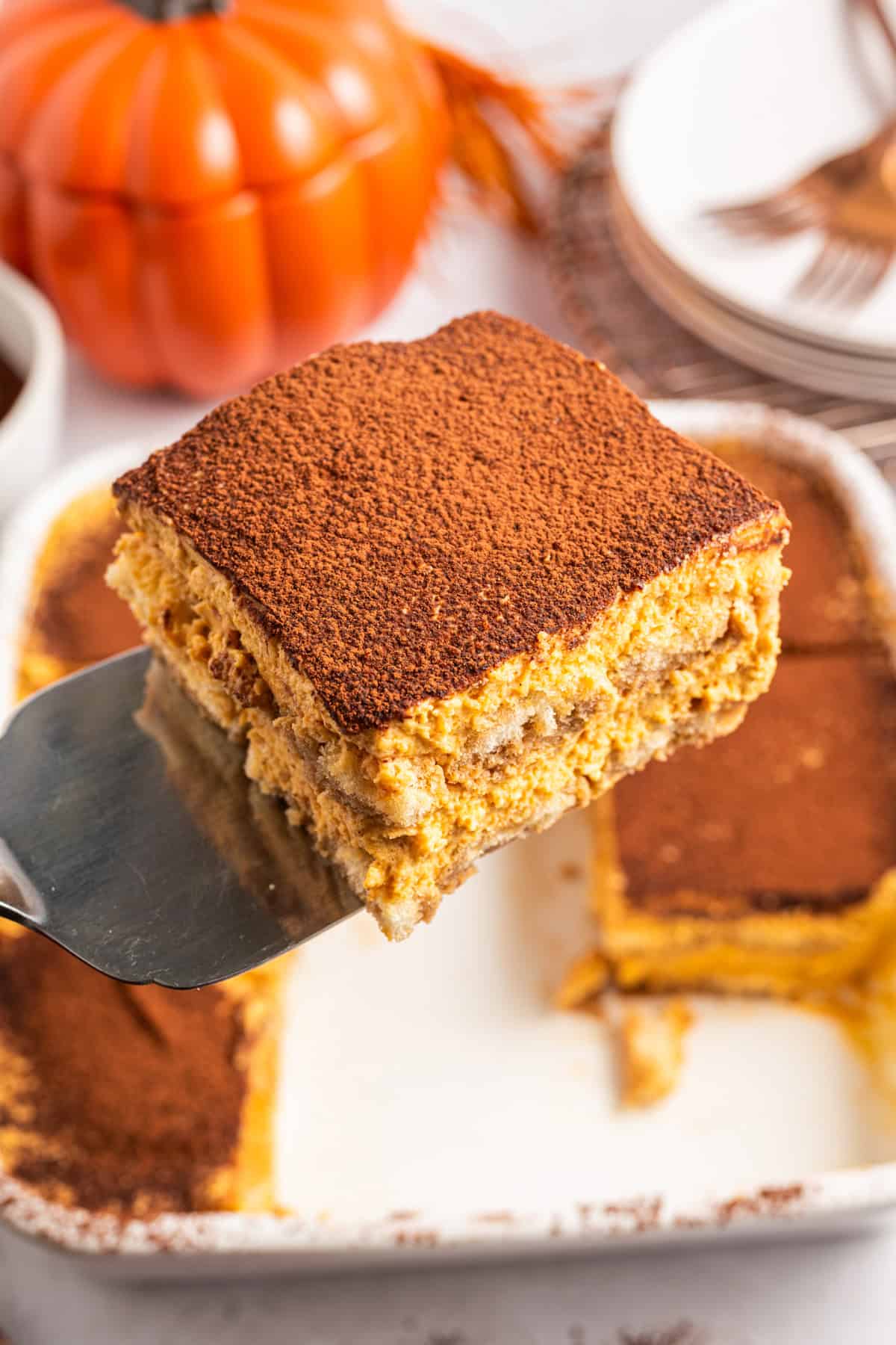 Pumpkin Tiramisu A slice of pumpkin tiramisu dusted with cocoa powder being lifted from a baking dish.