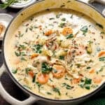 Creamy vegetable soup in a large pot, filled with sliced carrots, spinach, mushrooms, and herbs, garnished with black pepper and red pepper flakes.