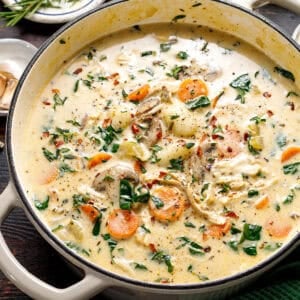 Creamy vegetable soup in a large pot, filled with sliced carrots, spinach, mushrooms, and herbs, garnished with black pepper and red pepper flakes.