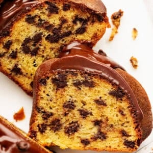Close-up of two slices of chocolate chip bundt cake with chocolate glaze drizzled on top, showing a moist yellow cake with visible chocolate chips.