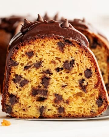 A close-up of a chocolate chip bundt cake slice topped with chocolate glaze and chocolate chips, showing a moist, golden interior with plenty of chocolate chips.
