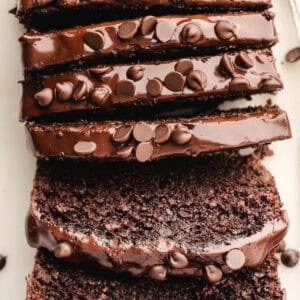 Sliced chocolate loaf cake topped with glossy chocolate frosting and chocolate chips.