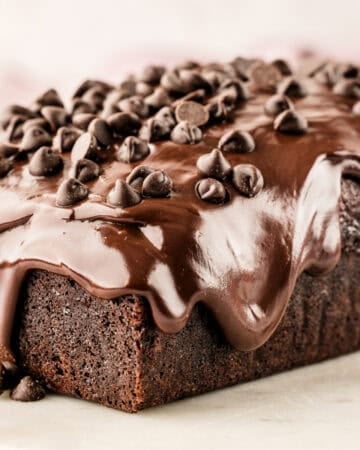 A rich chocolate loaf cake topped with glossy chocolate icing and sprinkled with chocolate chips.