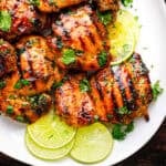 Grilled chicken thighs glazed with sauce, garnished with chopped cilantro, and served on a white plate with fresh lime slices.