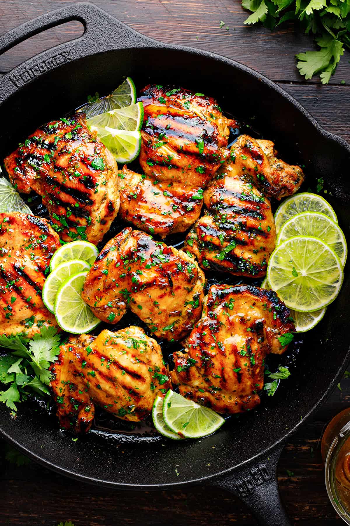 Cilantro Lime Chicken Grilled chicken thighs with char marks in a cast iron skillet, garnished with fresh lime slices and chopped cilantro.