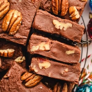 Close-up of chocolate fudge squares topped and filled with pecan halves, stacked on a wire rack.