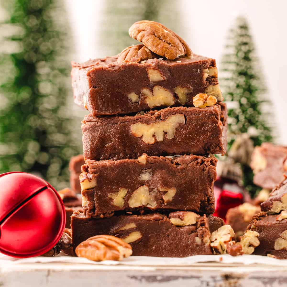 Four pieces of chocolate fudge with nuts are stacked on a wooden surface, garnished with pecans.