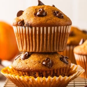 Two pumpkin chocolate chip muffins are stacked on top of each other, with chocolate chips visible on top.