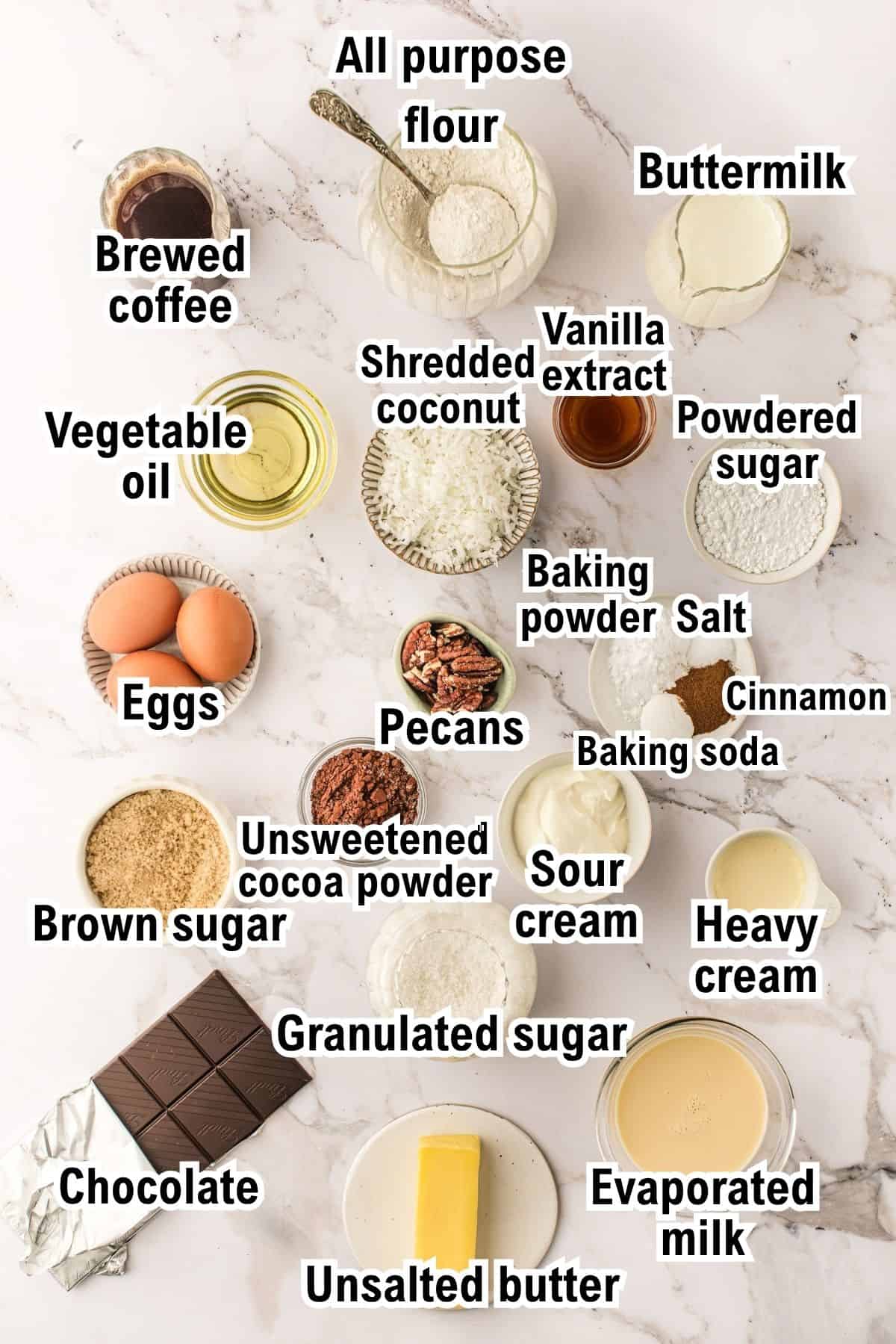 The Ingredients for German Chocolate Cake This photo shows the ingredients for German Chocolate Cake including flour, buttermilk, coffee, oil, eggs, sugars, coconut, nuts, cocoa, cream, baking agents, vanilla, salt, cinnamon, evaporated milk, chocolate, and butter on a marble surface.
